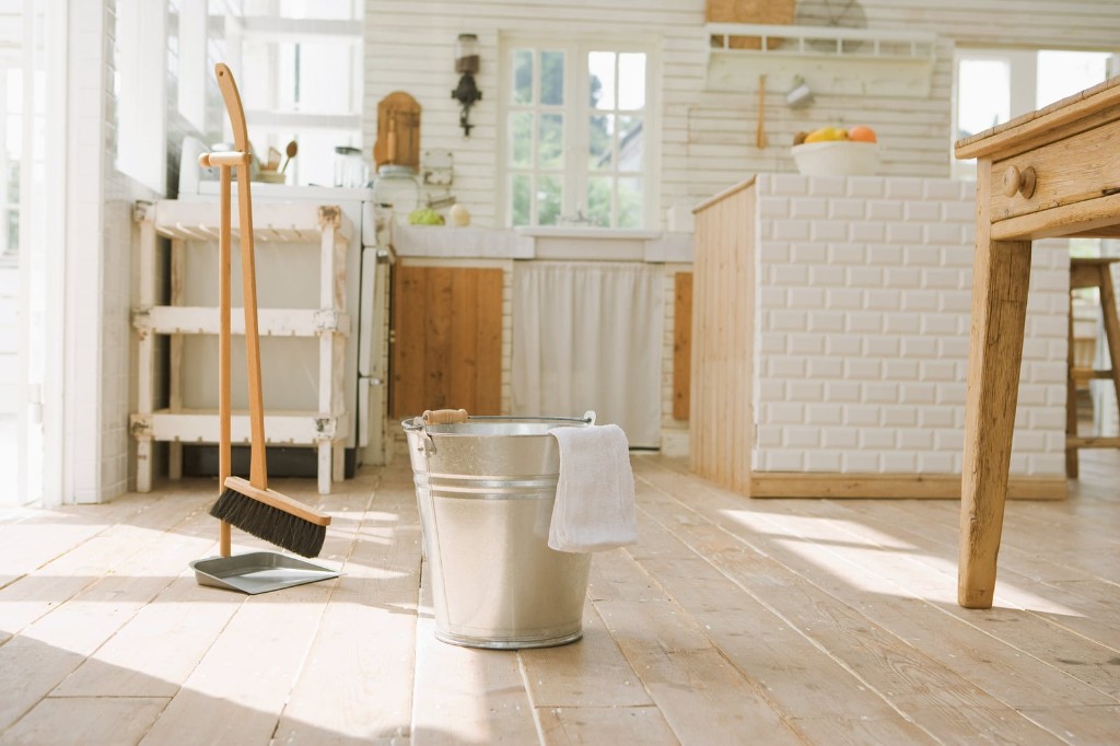 Galvanized bucket and broom on light wood floors in a bright rustic kitchen