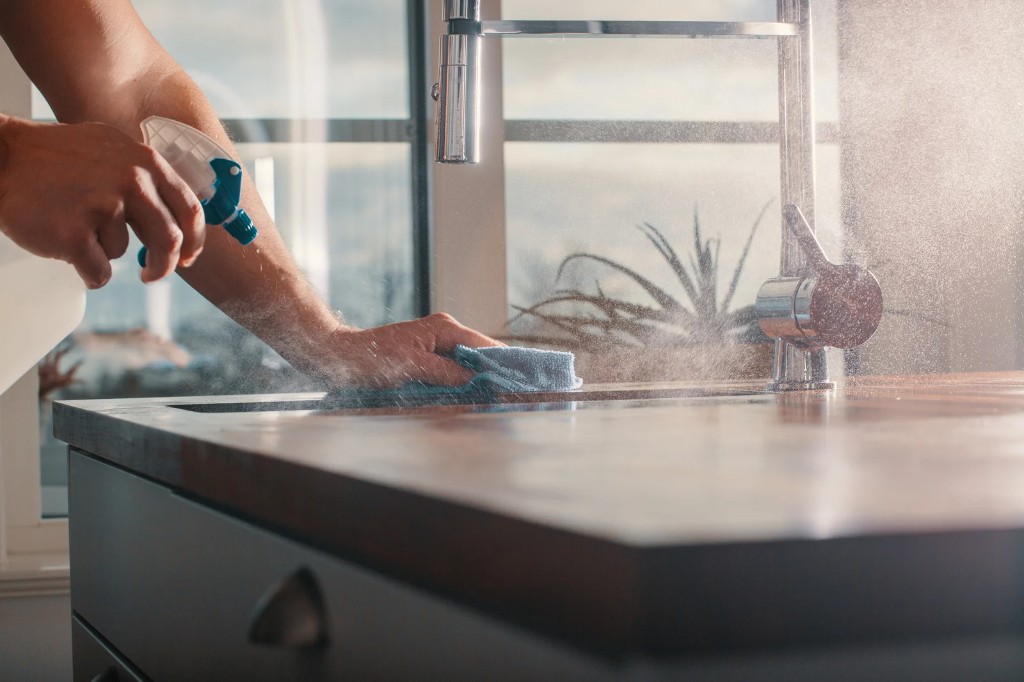 Hands spraying and wiping a kitchen countertop with a microfiber cloth